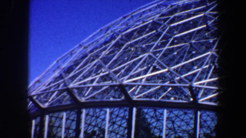 1964 Saint Louis home-movie frame showing triangular steel dome trusses seen from below against clear blue sky.