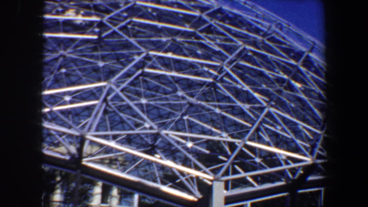 1964 Saint Louis home-movie frame showing a white metal geodesic dome roof with dense triangular latticework against blue sky.