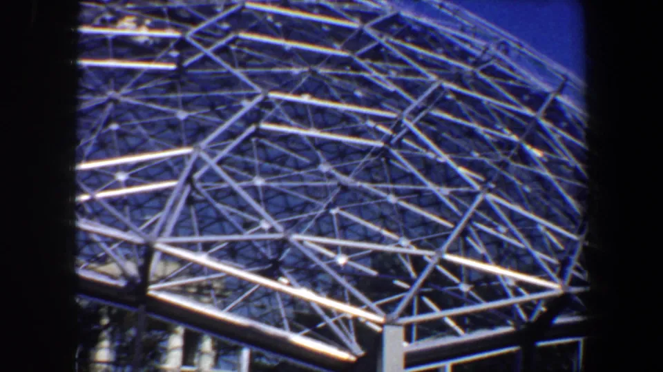 1964 Saint Louis home-movie frame showing a white metal geodesic dome roof with dense triangular latticework against blue sky.