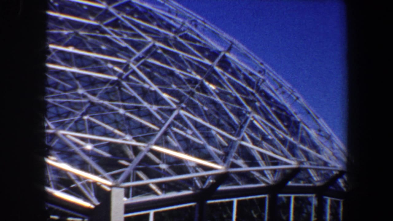 Curved geodesic dome roof with white lattice beams and blue sky.