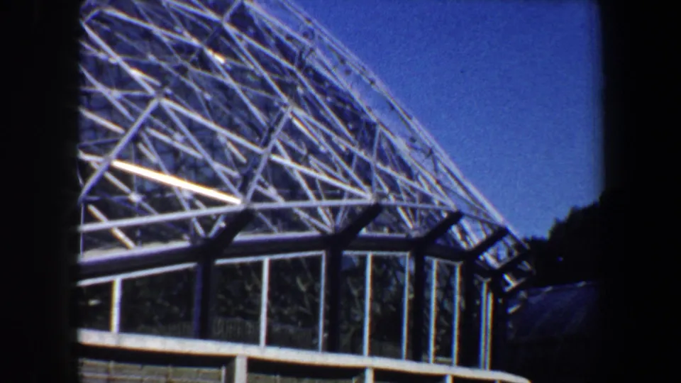 1964 Saint Louis home-movie view of a geodesic dome over glass wall panels, with white structural beams and blue sky.