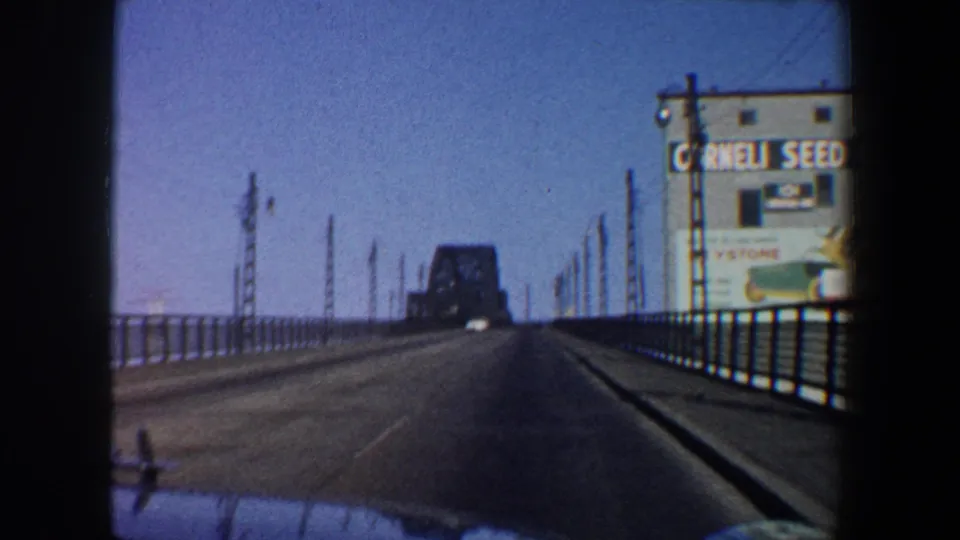 1964 Saint Louis car-window view along a bridge, showing railings, utility poles, a distant bridge form, and Cornell Seed Co. signage.