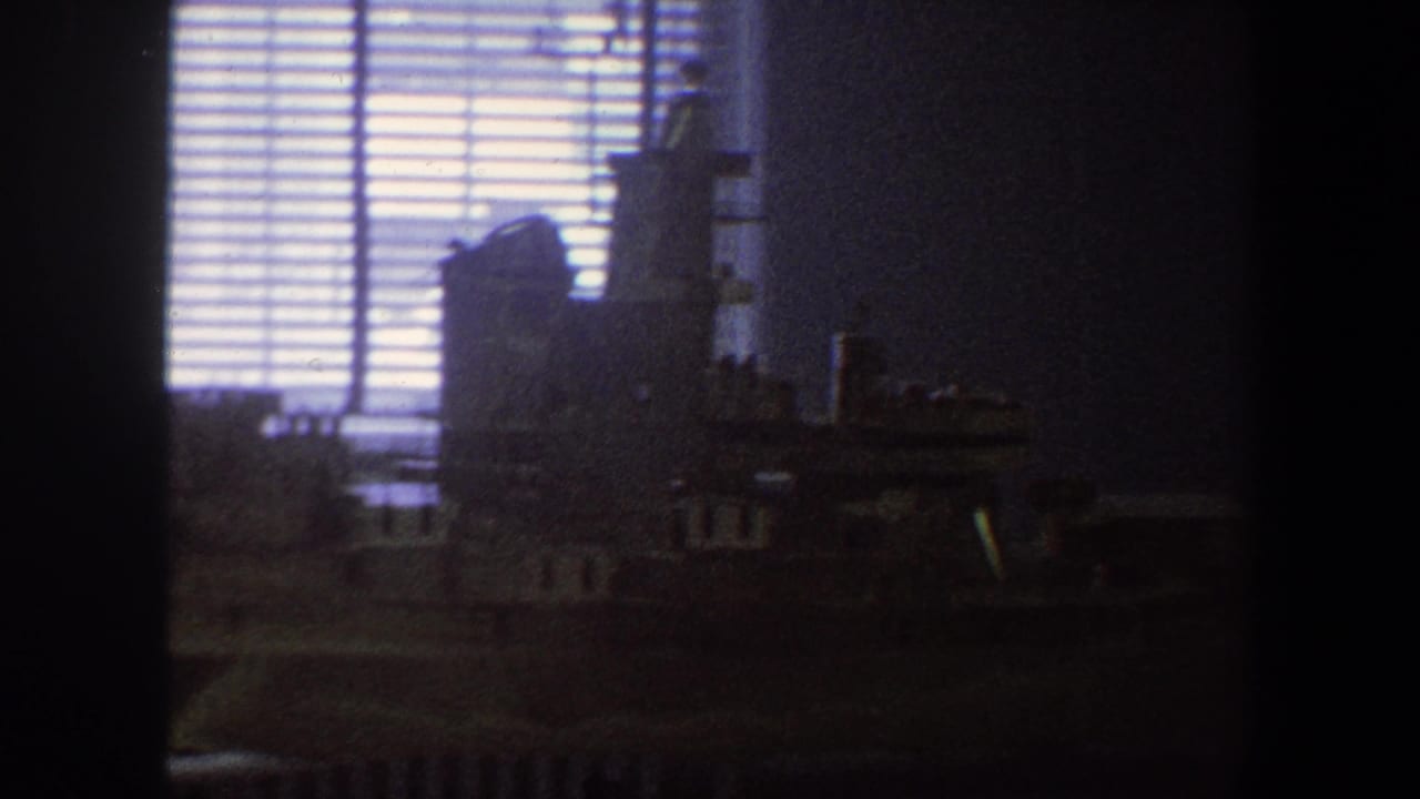 1964 Saint Louis home-movie frame showing a dim room, window blinds, and a shadowed model naval ship on a table.