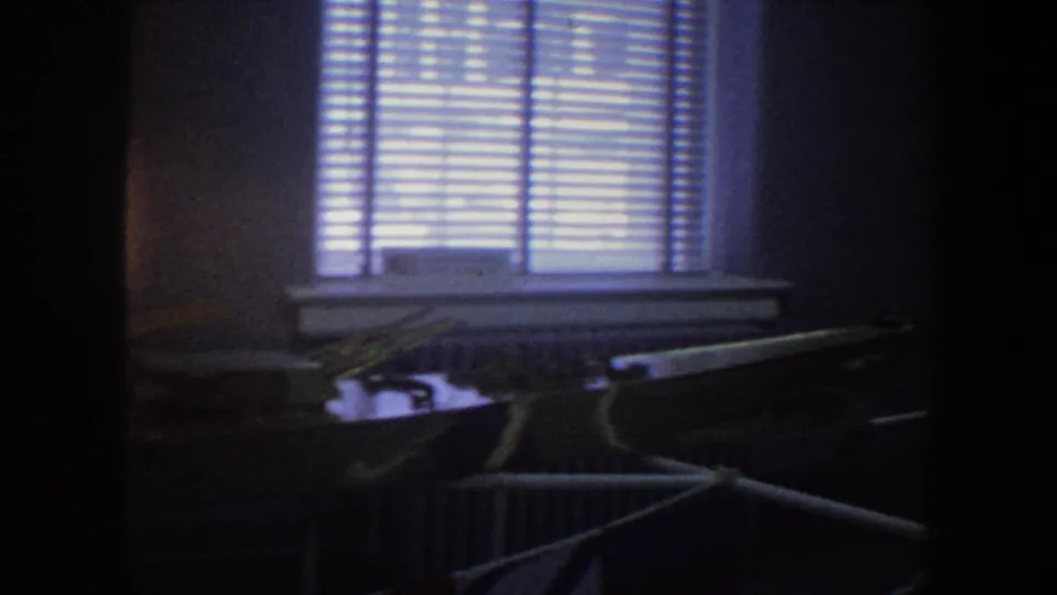 Dim 1964 Saint Louis interior frame showing venetian blinds, a radiator, and the length of a model naval ship in low light.