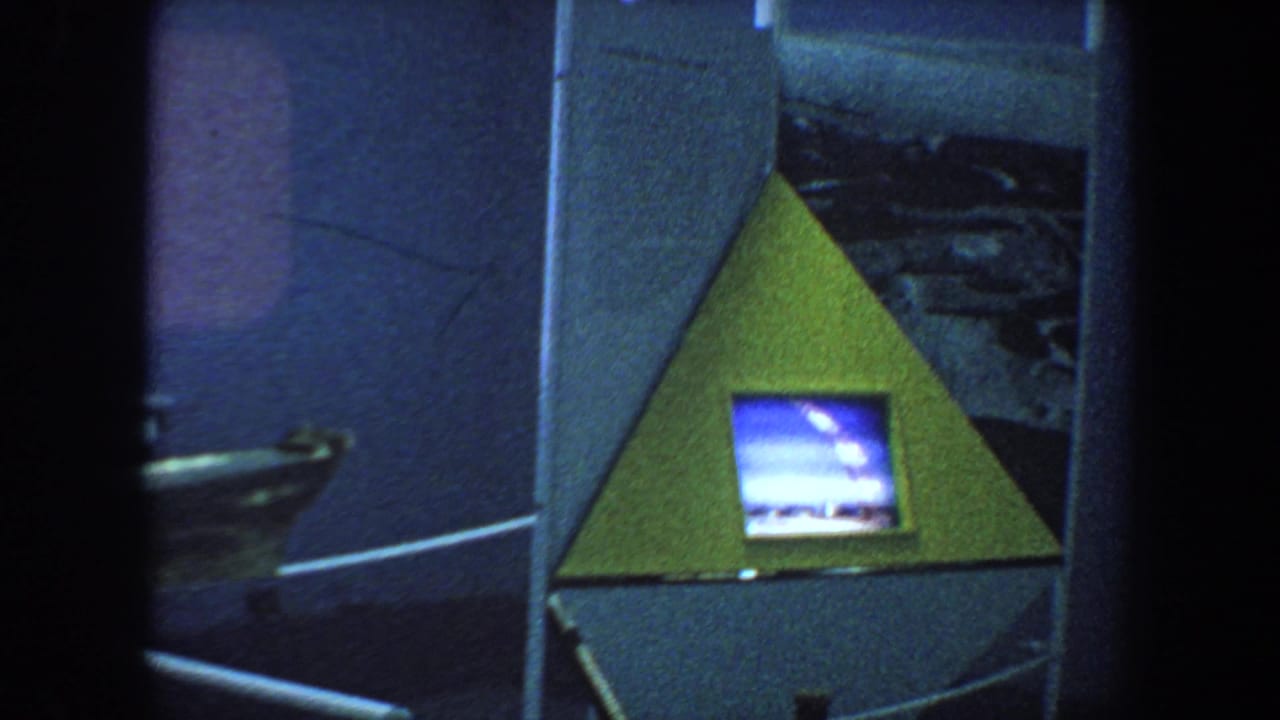 Triangular museum-style display with a small glowing television screen in a dark interior.