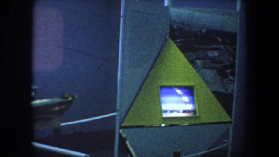 1964 8mm frame showing a triangular exhibit structure with a small blue-toned television screen inside a dim display area.