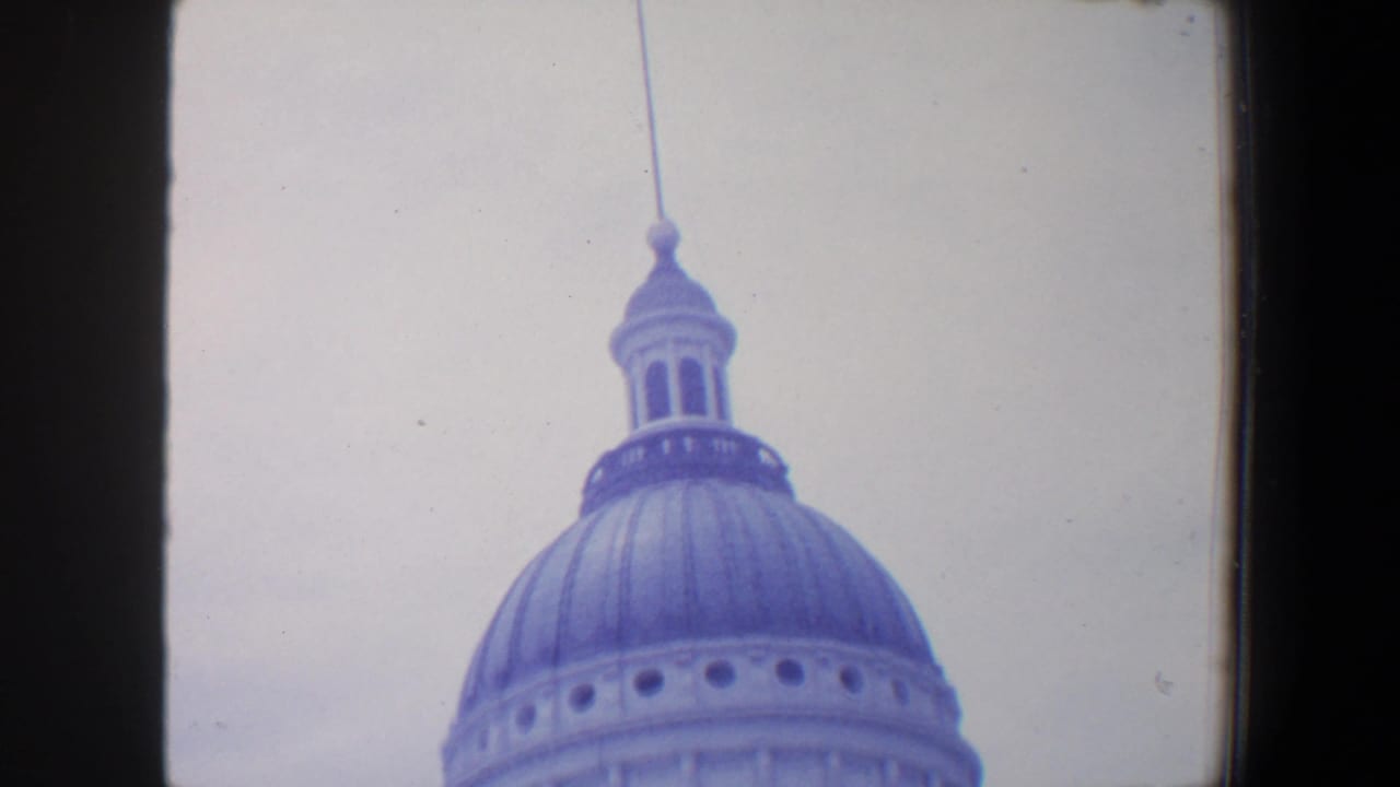 1964 8mm frame showing the upper portion of a large domed civic-looking building, possibly in Missouri, against a bright pale sky.