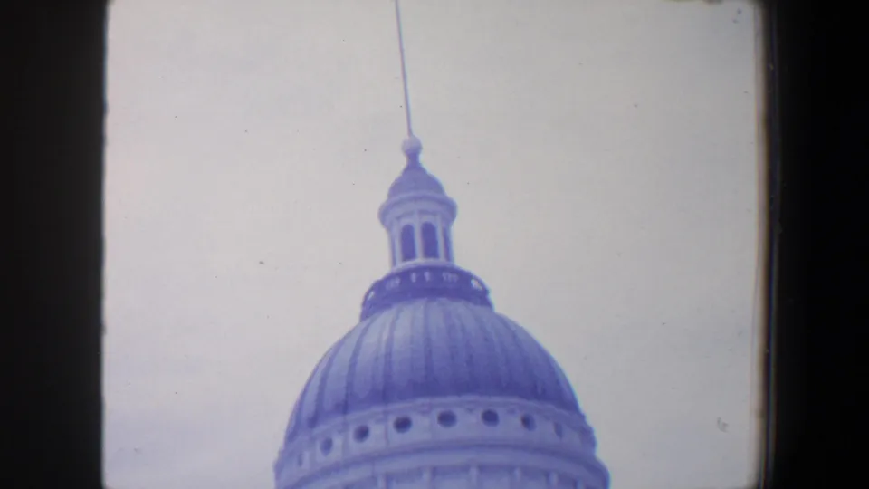 1964 8mm frame showing the upper portion of a large domed civic-looking building, possibly in Missouri, against a bright pale sky.