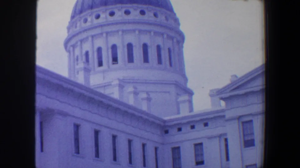 1964 8mm frame showing a domed civic-looking building exterior with rectangular windows, rooflines, and classical architectural details.
