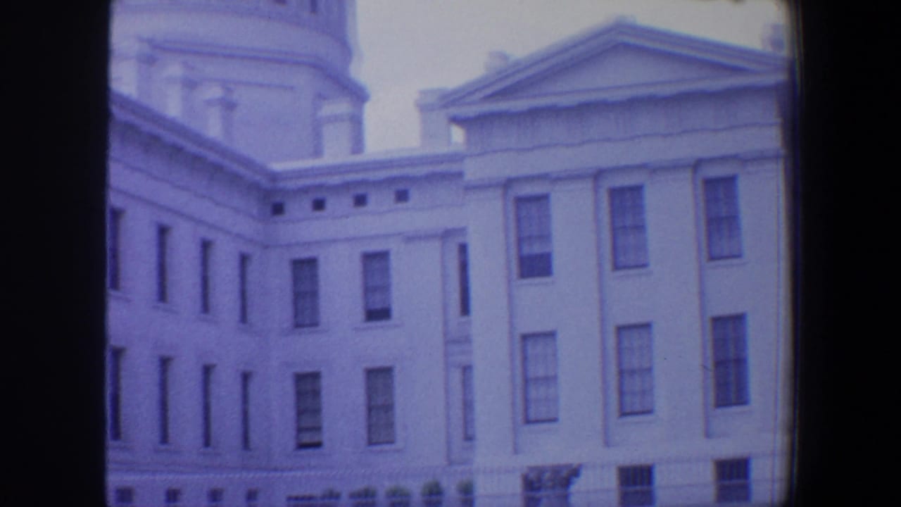 Classical white building facade with dome fragment, pediment, and rows of windows.