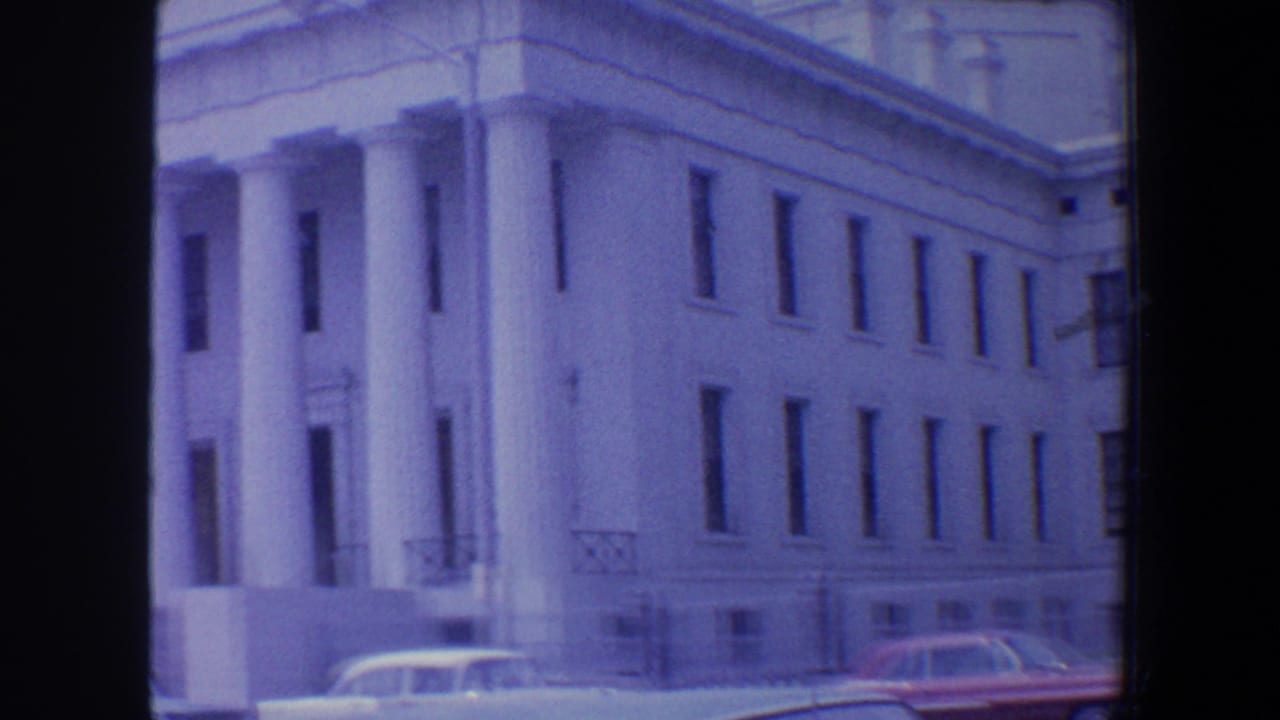 Columned entrance and side wall of a white classical building with cars below.