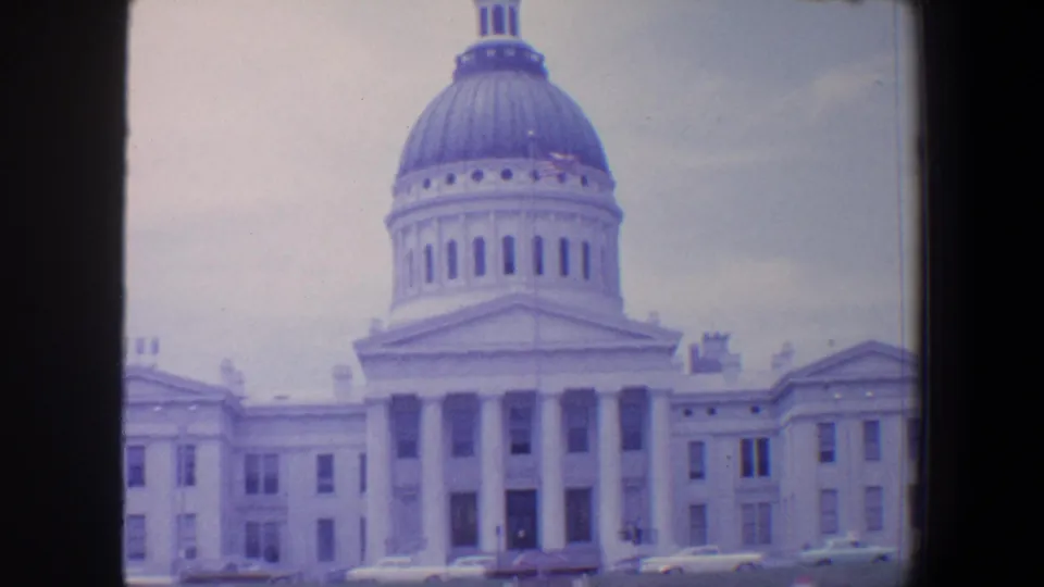 1964 Saint Louis home-movie view of a domed white civic building with columns, lawn, and period cars along the foreground.