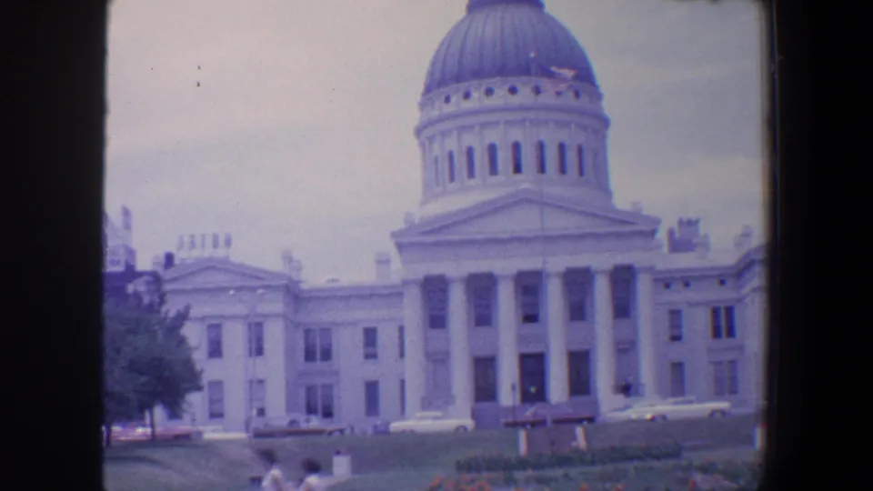 1964 Saint Louis frame showing the domed public building across a lawn, with parked cars and small distant pedestrians in the foreground.