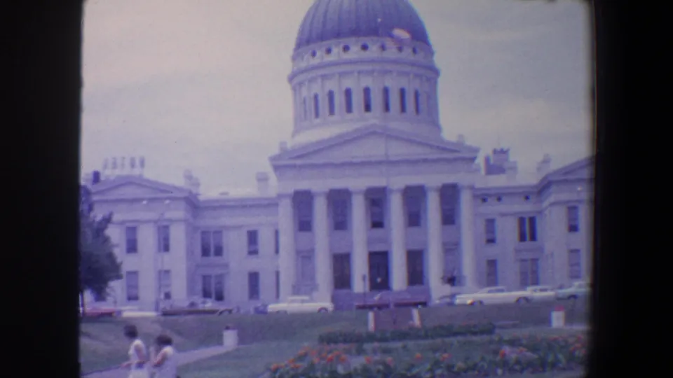 1964 8mm view in Saint Louis showing a domed columned civic building, landscaped grounds, parked cars, and distant pedestrians.