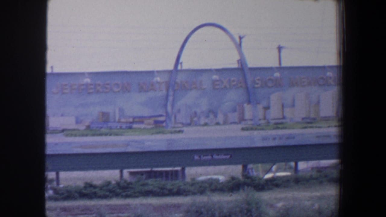 Roadside memorial billboard with Gateway Arch artwork, skyline illustration, and dark film frame edges.
