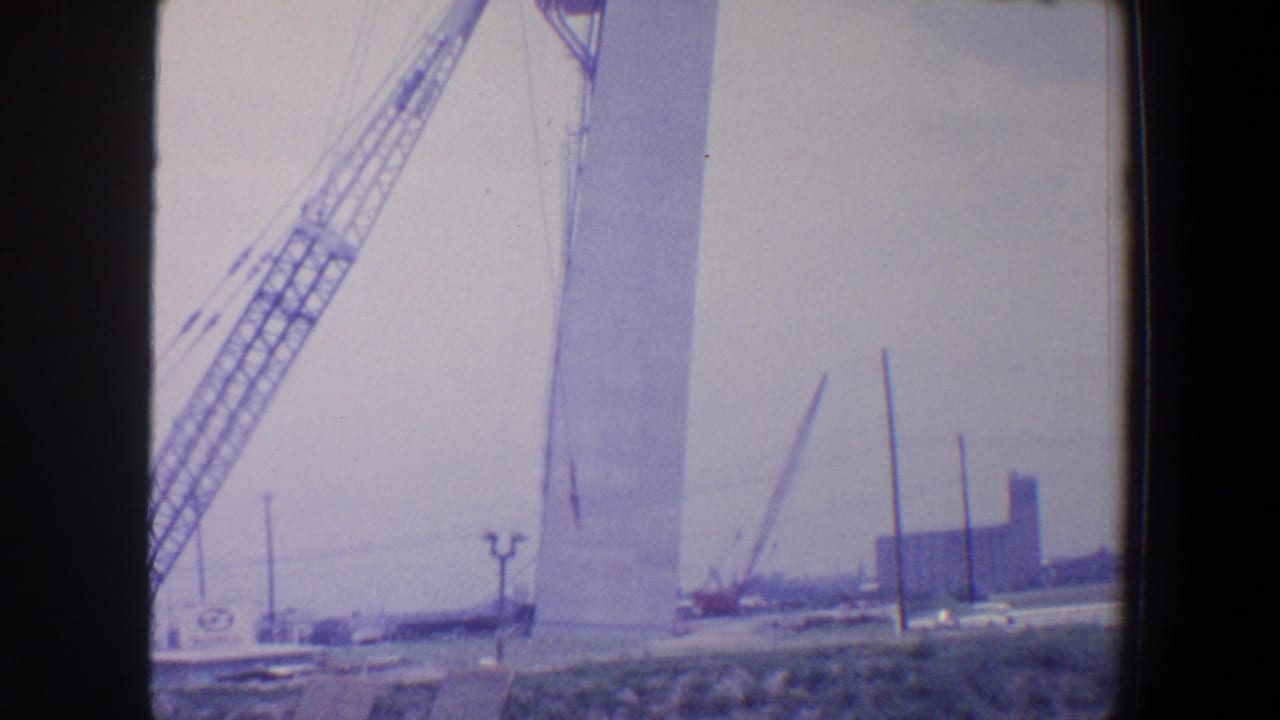 Tall pale structure with cranes and worksite equipment in the distance.