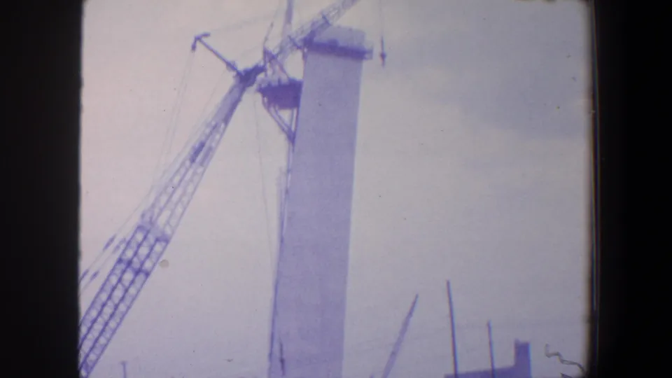 1964 Saint Louis 8mm frame showing a lattice crane working near a tall Gateway Arch segment against a pale sky.