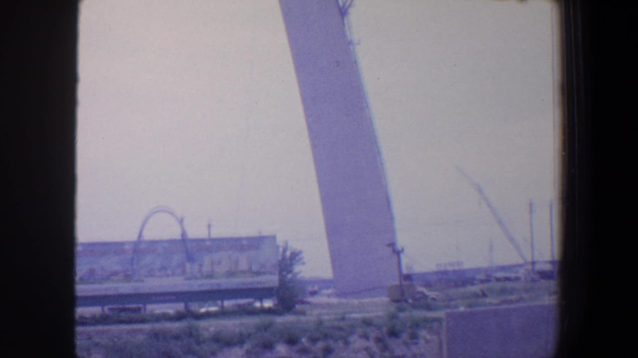 Gateway Arch curve in the background with construction equipment and low buildings in front.