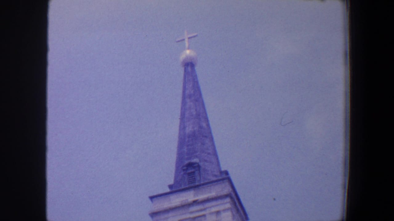 Church steeple with cross and part of the tower framed against blue sky.