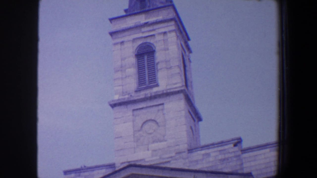 1964 Saint Louis 8mm frame showing the upper section of a pale stone religious tower with louvered opening and soft purple film cast.