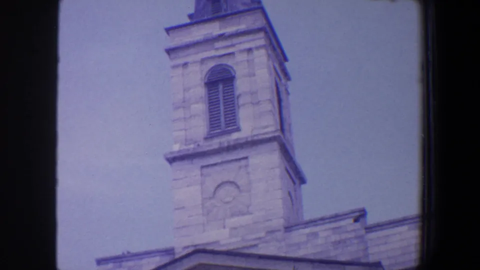 1964 Saint Louis 8mm frame showing the upper section of a pale stone religious tower with louvered opening and soft purple film cast.