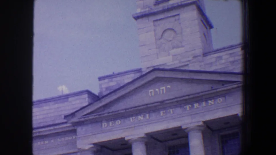 1964 Saint Louis 8mm view of a religious facade with tower, pediment, columns, Hebrew letters, and Latin inscription visible through film grain.