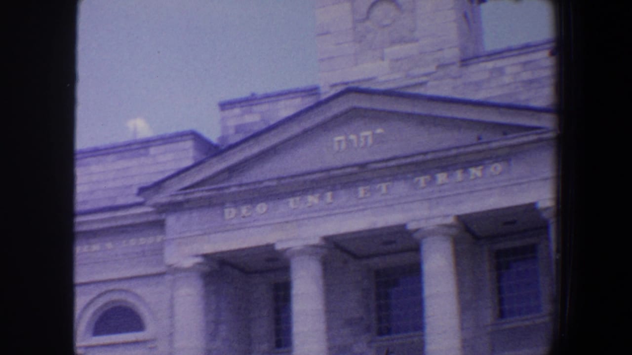 Neoclassical stone facade with columns, pediment lettering, and an arched window.