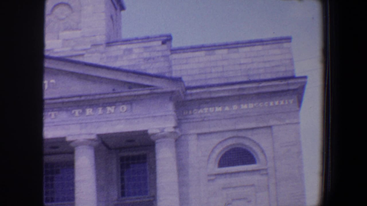 Upper facade with pediment, columns, Latin inscription, and arched window.