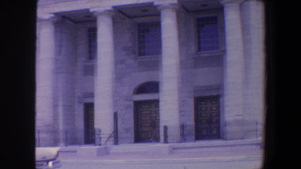 1964 Saint Louis home-movie view of a stone building with large columns, wooden doors, tall windows, steps, and a street curb.