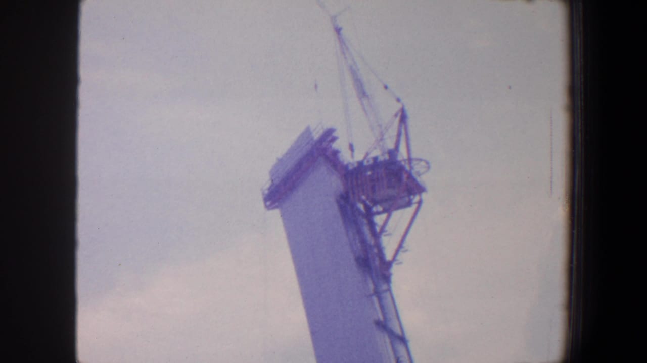 Tall tapered church tower under construction with crane rigging against a pale sky.