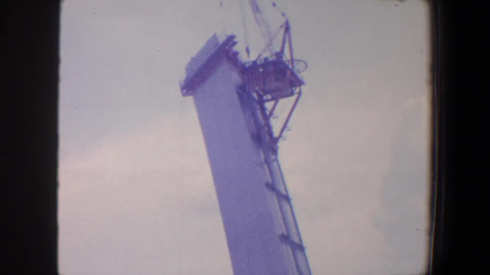 1964 Saint Louis frame showing the upper tower structure, crane cables, and exposed platform near the top of the church construction.