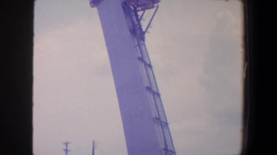 1964 Saint Louis home-movie frame with the tower side filling the view, showing ladder-like staging and rigging near the top.