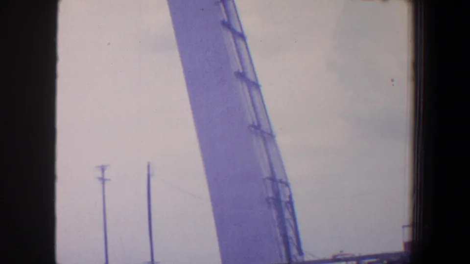 1964 Saint Louis frame showing the church tower under construction, with ladder-like staging, crane structure, and utility poles below.