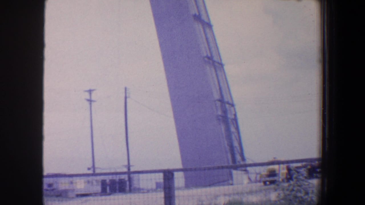 Utility poles and a large angled structure behind a fence, with dark vertical framing in the foreground.