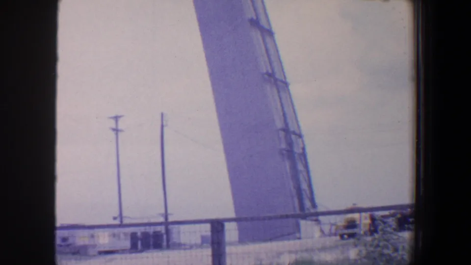 1964 Saint Louis view of utility poles, fencing, and a large angled industrial structure seen from behind a dark vertical frame.