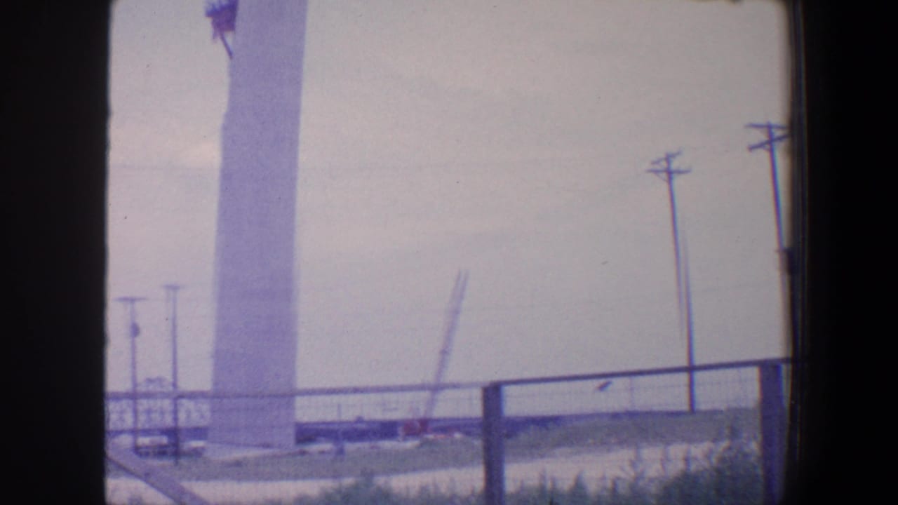 Tall white column under construction with crane, railing, utility poles, and power lines.
