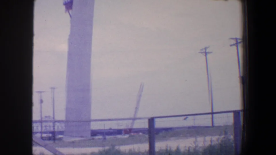 1964 Saint Louis 8mm frame showing a tall white column under construction behind railing and power lines.