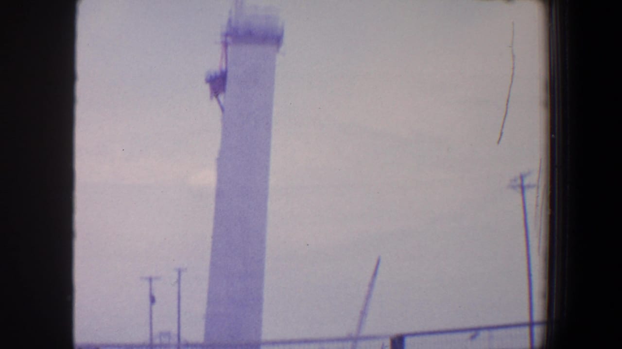Upper portion of a tall white column with crane equipment and utility poles nearby.