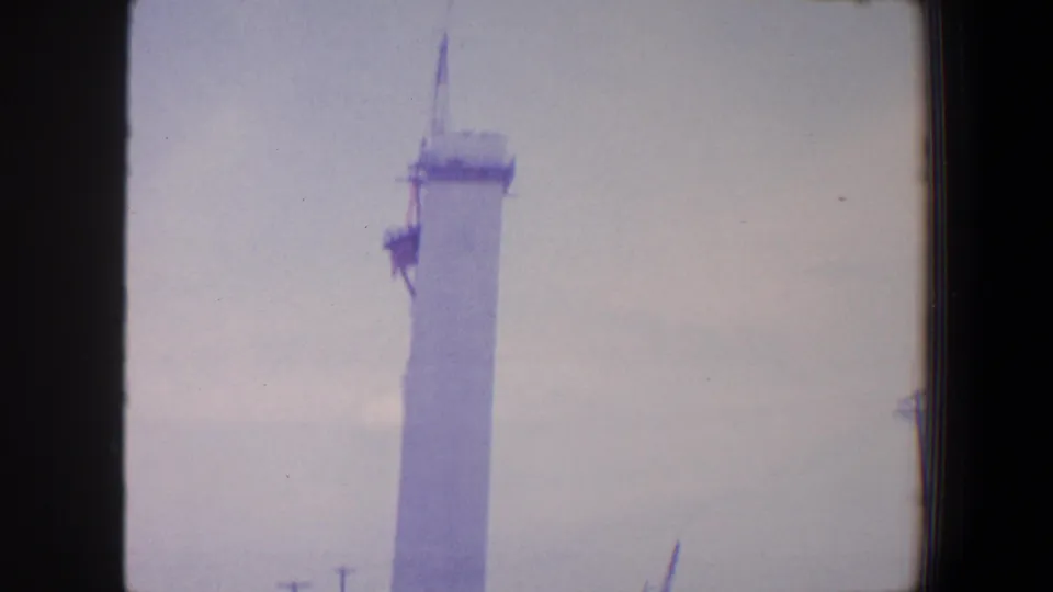 1964 Saint Louis 8mm still with a tall white column, crane boom, faint railing, and open sky.