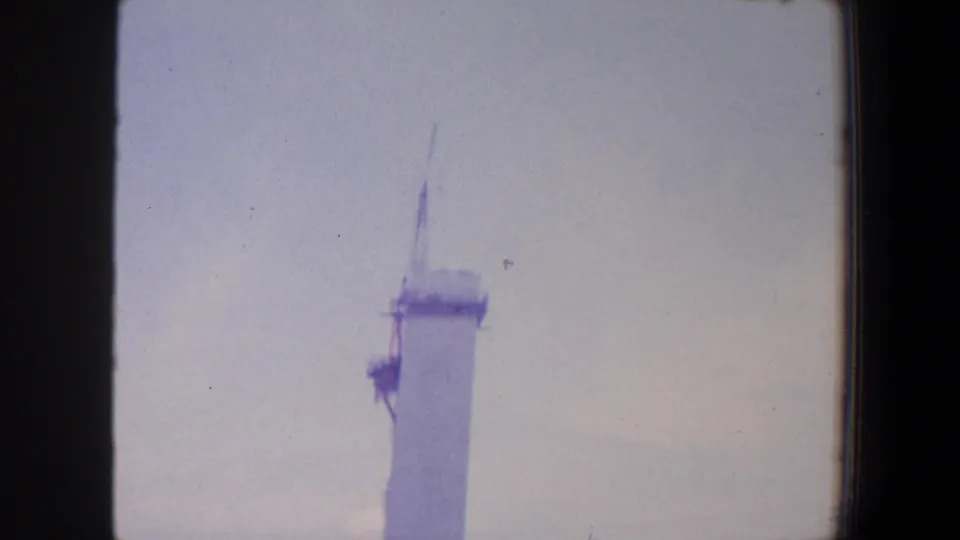 1964 Saint Louis home-movie frame showing the column top and crane boom, with utility poles near the edge.