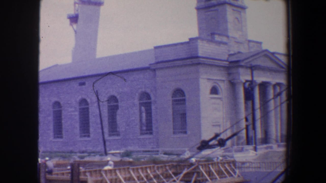 Side view of stone church with arched windows, tower, scaffolding, and parked cars.