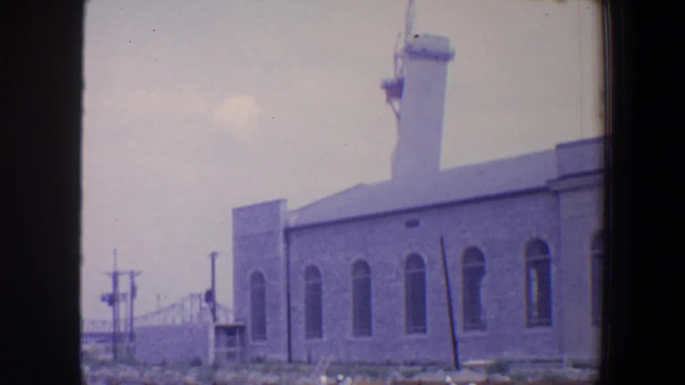 1964 Saint Louis home-movie frame showing a towered industrial building with arched windows and utility poles in front.