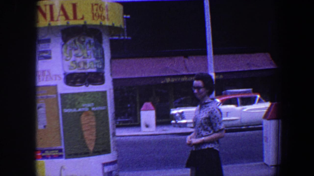 Woman walking past a yellow and white Centennial booth on a city street.