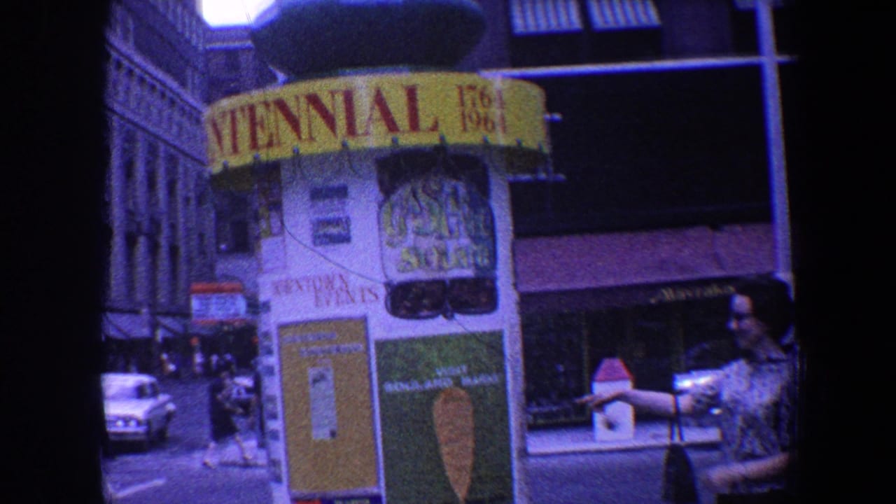 Centennial booth near storefronts and cars, with a woman at the right edge.