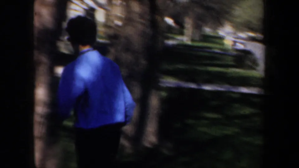 Wyoming 1957 frame showing a person in a bright blue jacket moving across a residential lawn during departure activity.