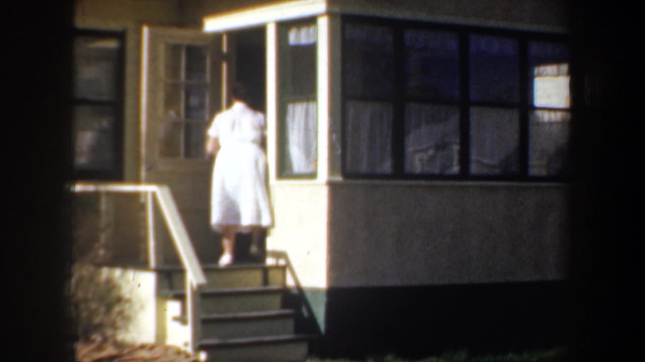 Woman in white dress stands at the doorway while entering the house.