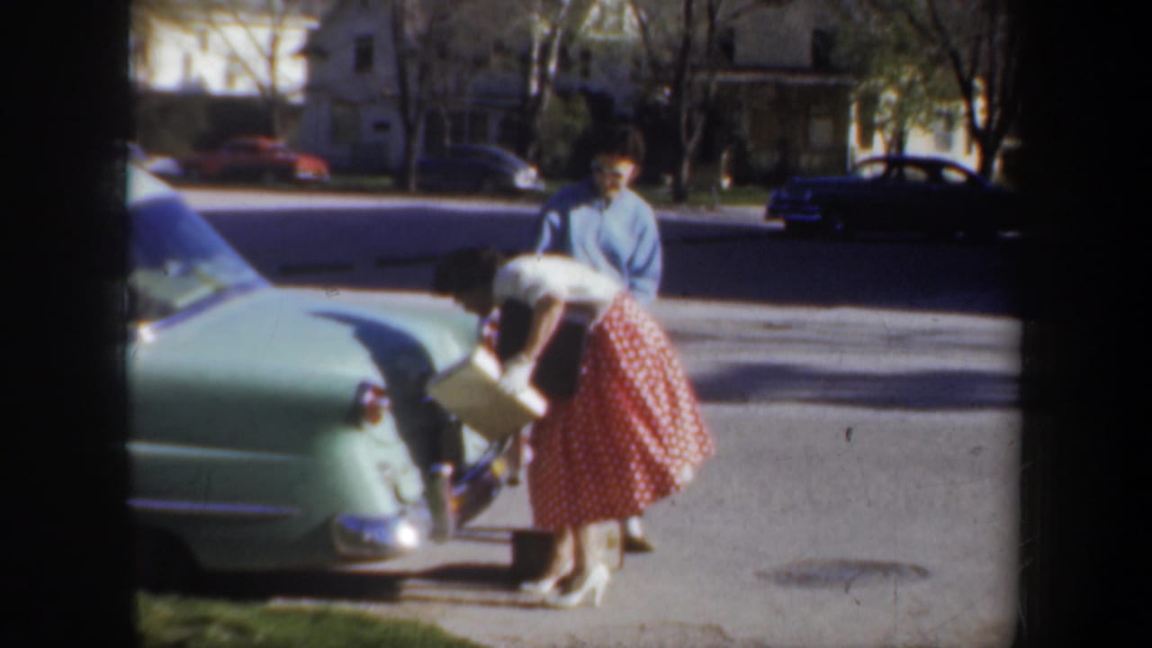The woman continues trying to manage the trunk or rear compartment of the green car while the man looks on in the Wyoming street scene.