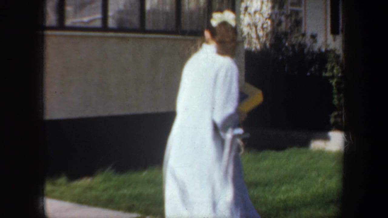 Woman seen from behind walks along a path beside a lawn and house.