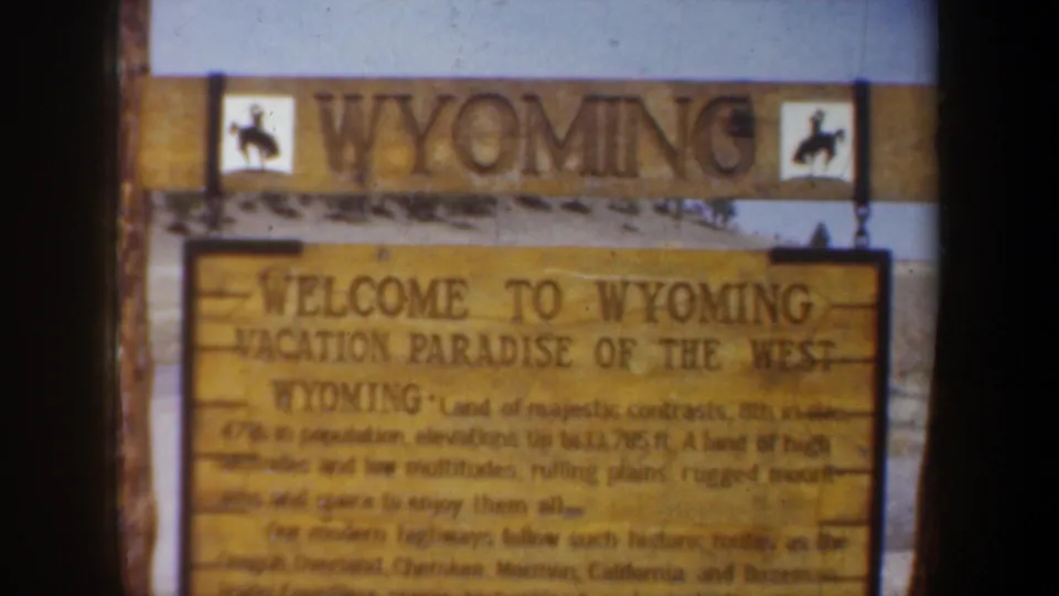 A wooden Welcome to Wyoming sign fills the frame, with smaller tourism text visible but partly soft from the 8mm scan.