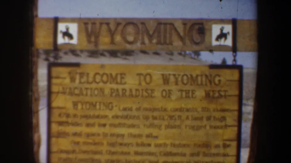 Closer 8mm view of the Welcome to Wyoming sign, including the phrase Vacation Paradise of the West and surrounding wood structure.